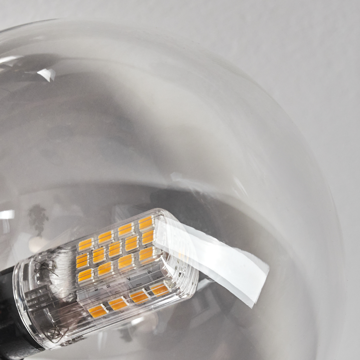 Nahaufnahme einer klaren Glühbirne mit LED-Modul. Die LED hat orangefarbene Lichter. Der Hintergrund ist eine hellgraue Wand.