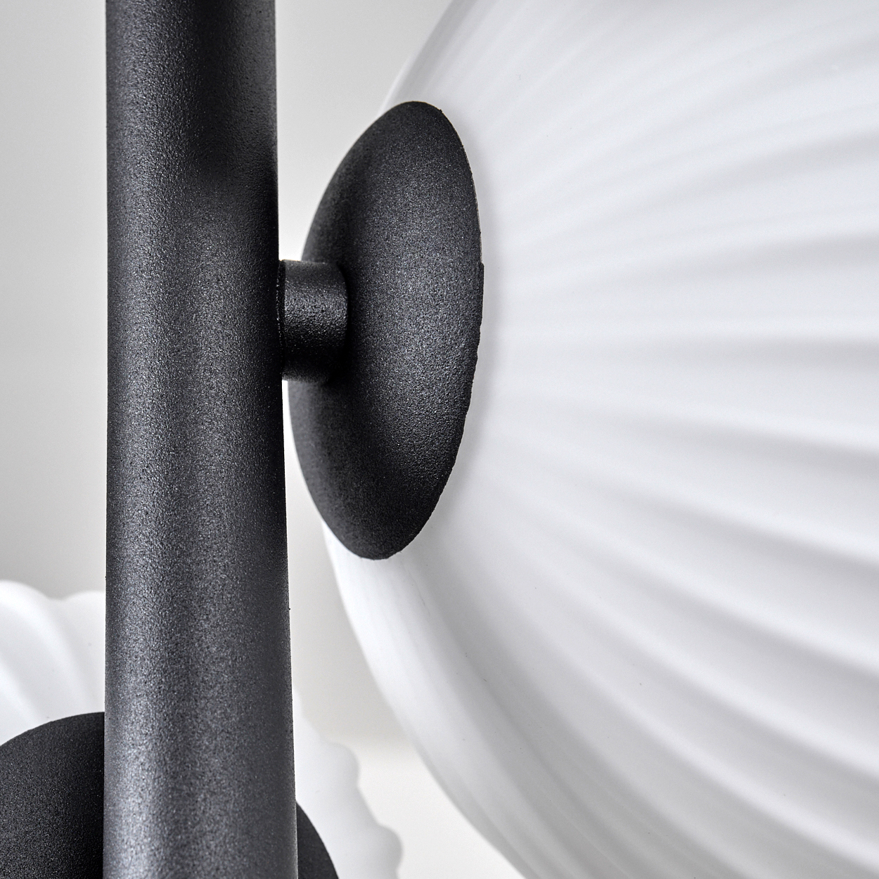 Nahaufnahme einer modernen Lampe. Sie hat einen schwarzen Metallrahmen und eine weiße, gerippte Glaskugel. Der Hintergrund ist weiss.