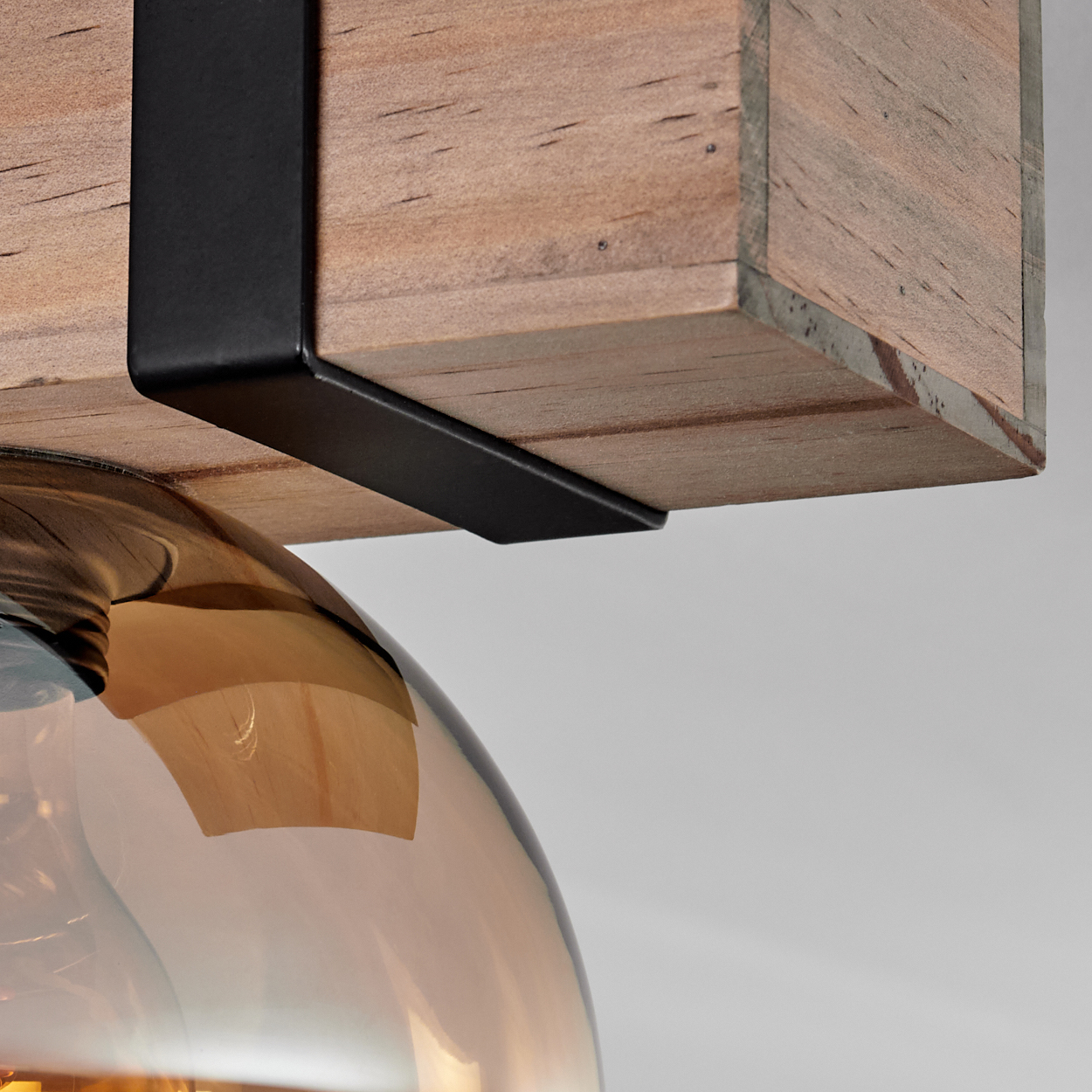 Nahaufnahme einer Leuchte. Ein Holzbalken wird von schwarzen Metallhalterungen gehalten. Unter dem Holz befindet sich eine Glühbirne.