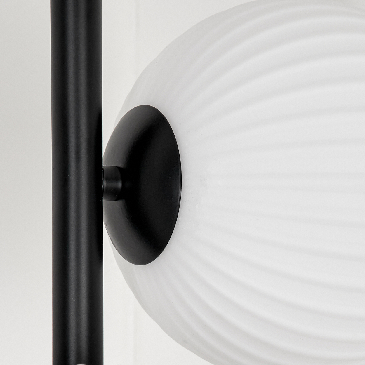Nahaufnahme eines schwarzen Lampenpfostens, der eine weiße, kugelförmige Lampe mit geriffelter Oberfläche hält. Der Hintergrund ist weiß.