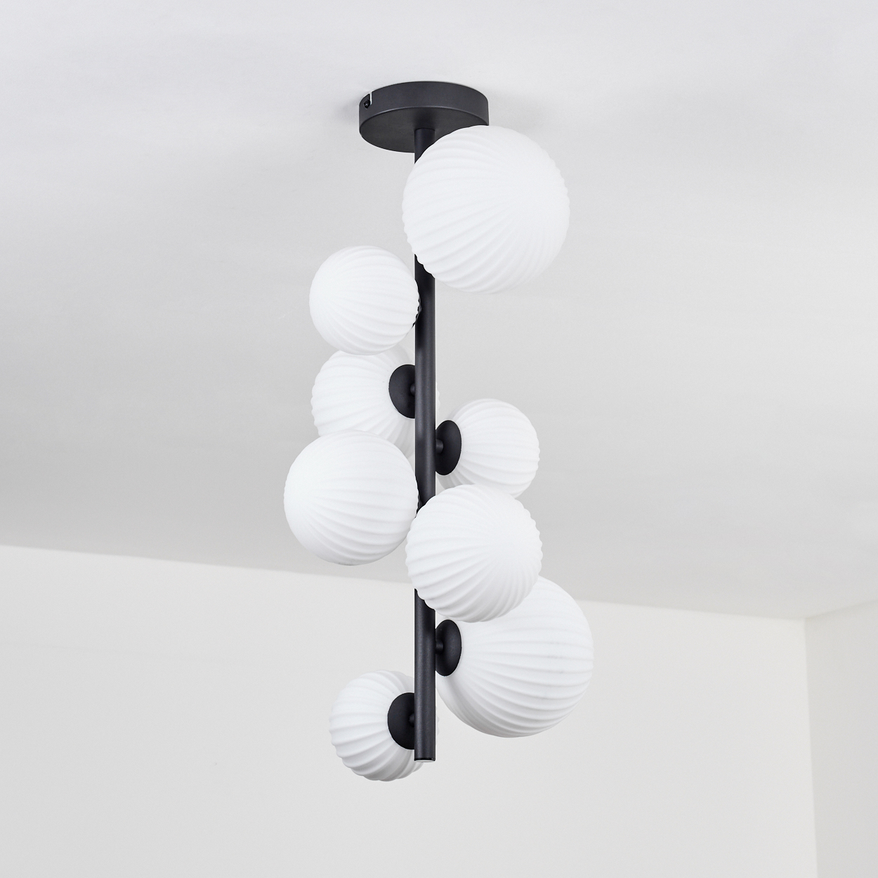 Eine schwarze, moderne Hängelampe mit weißen, strukturierten Kugeln, die von der Decke hängen. Der Hintergrund ist eine weiße Wand.