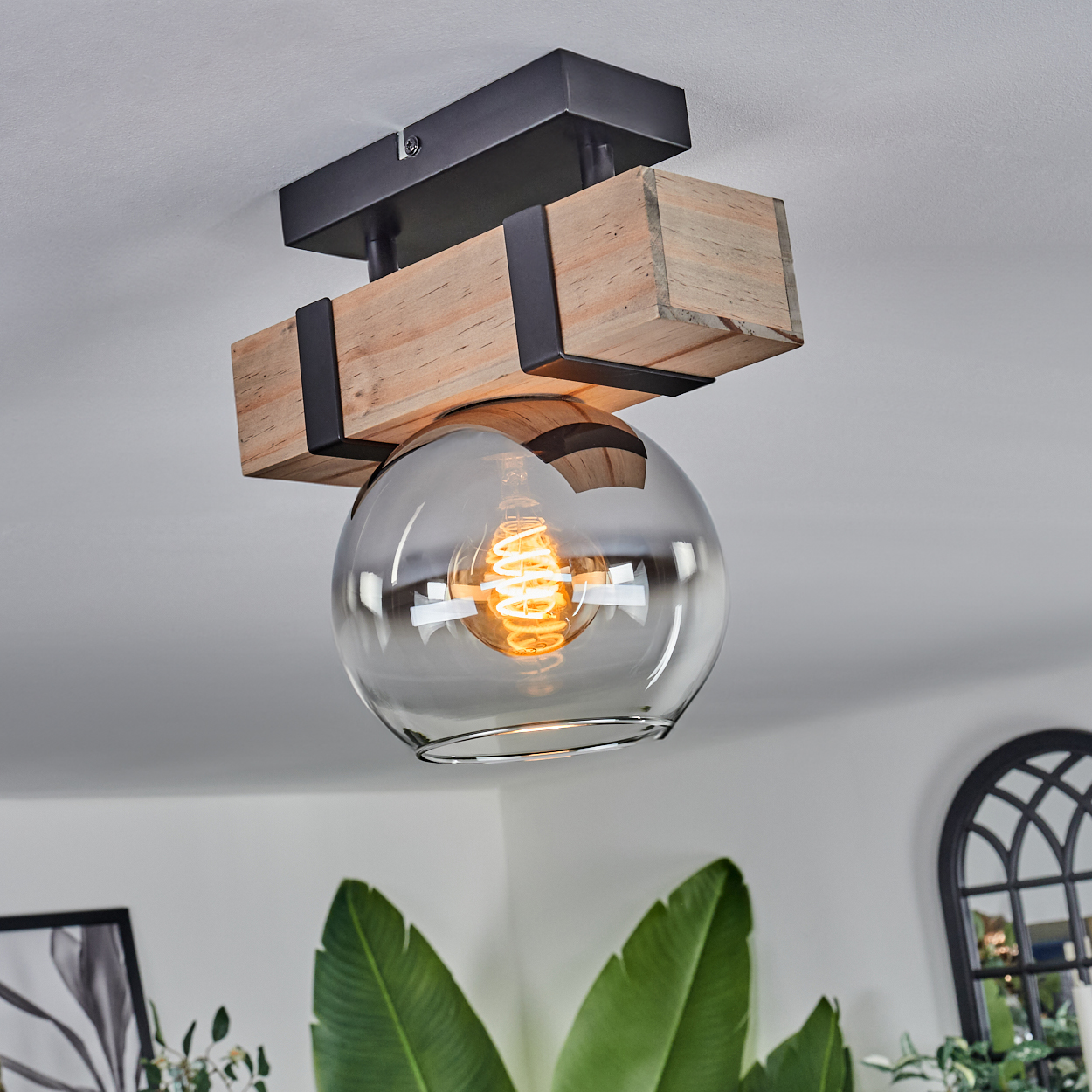 Eine Deckenleuchte mit Holz- und Metallrahmen, Glaskugel und einer leuchtenden Wendelbirne.