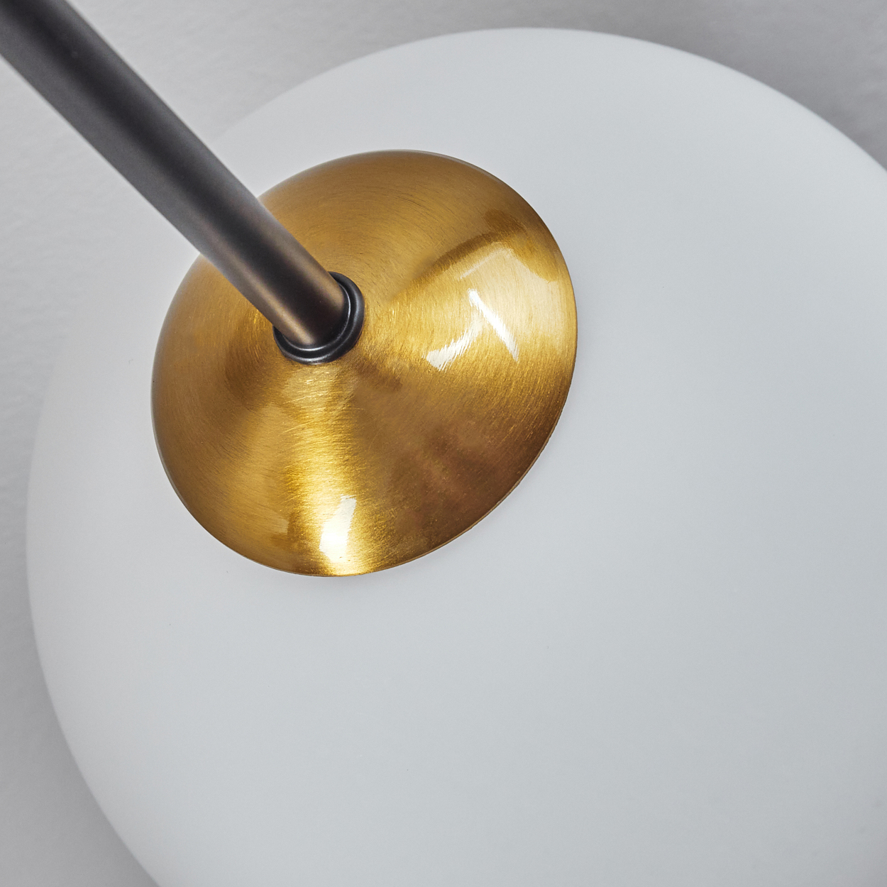 Nahaufnahme einer modernen Lampe. Sie hat einen goldenen Messingschirm, einen dunklen Metallarm und ein weißes kugelförmiges Glas.