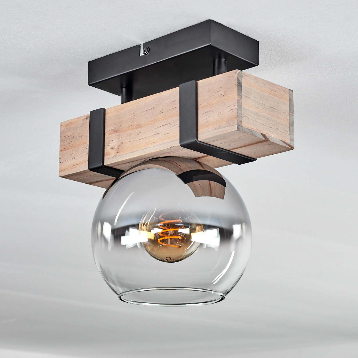 Moderne Deckenleuchte. Sie hat einen Holzbalken mit Glaskugel und einer sichtbaren Glühbirne. Die Leuchte ist an einer weißen Decke befestigt.