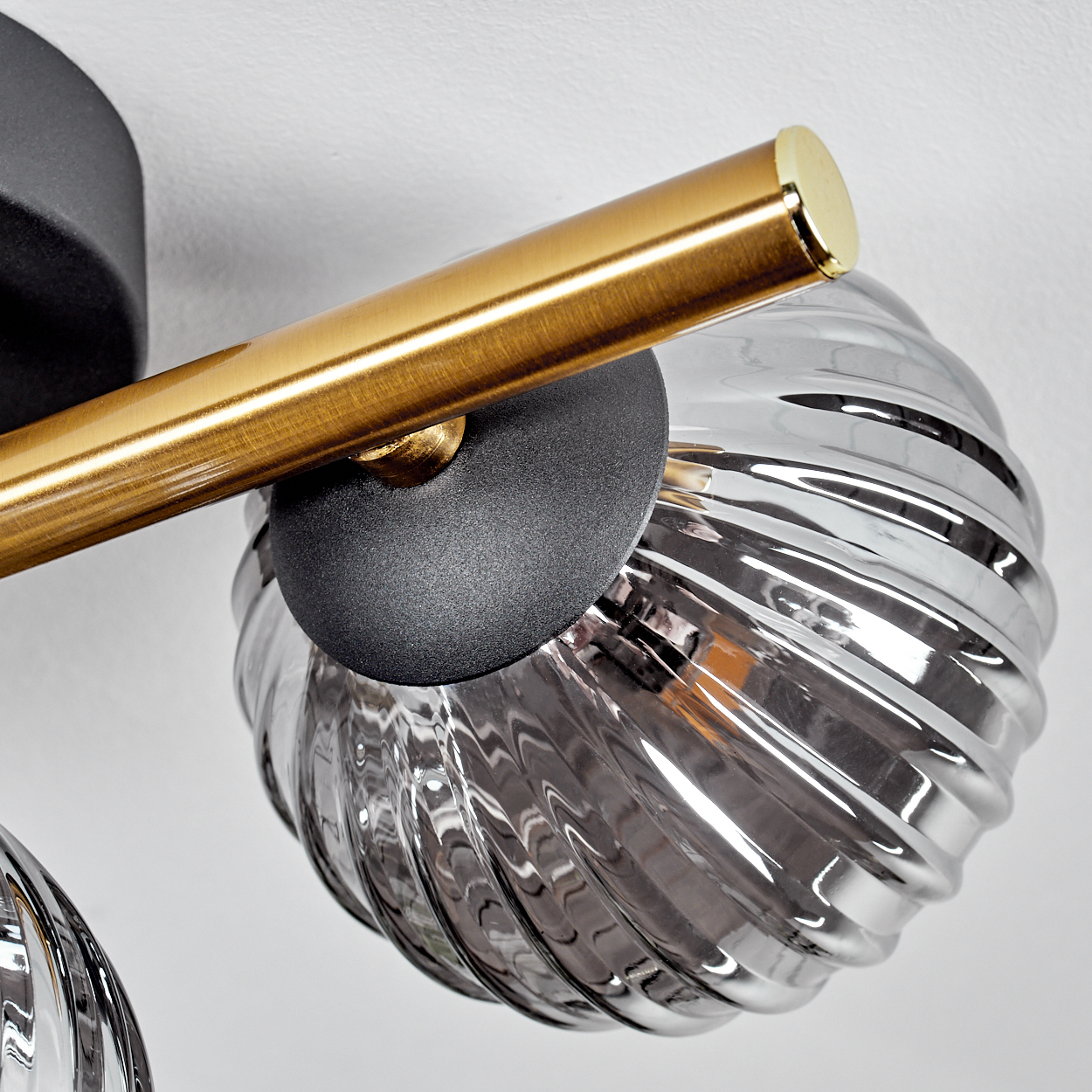Nahaufnahme einer modernen Leuchte. Sie hat einen goldenen Balken, einen silbernen Glaskolben und einen schwarzen Sockel auf weißem Grund.