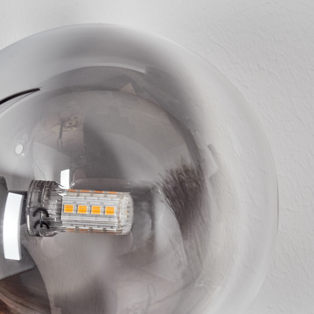 Nahaufnahme einer Glühbirne. Sie ist transparent mit sichtbarer LED und sitzt vor weißem strukturiertem Hintergrund.