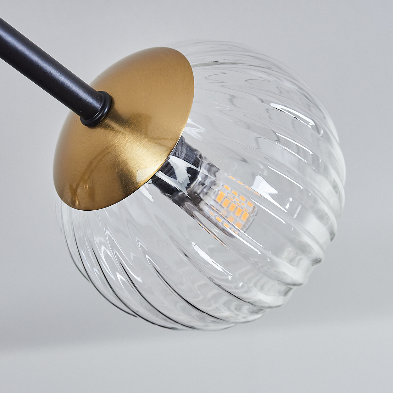 Nahaufnahme einer Glaskugelleuchte mit goldenem Deckel und schwarzem Arm. Die Kugel ist klar mit einem Spiraldesign.