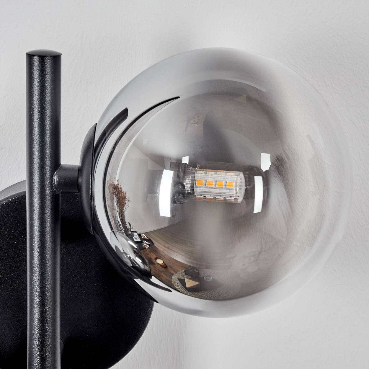 Eine moderne Wandlampe mit schwarzem Rahmen und einem klaren, kugelförmigen Glasschirm. Die Glühbirne ist im Schirm sichtbar.