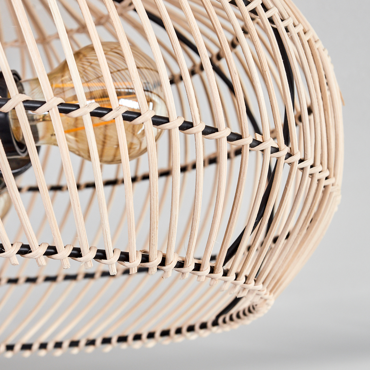 Nahaufnahme einer Pendelleuchte aus Rattan. Gewebter hellbrauner Schirm mit schwarzem Metallrahmen. Eine Glühbirne ist sichtbar.