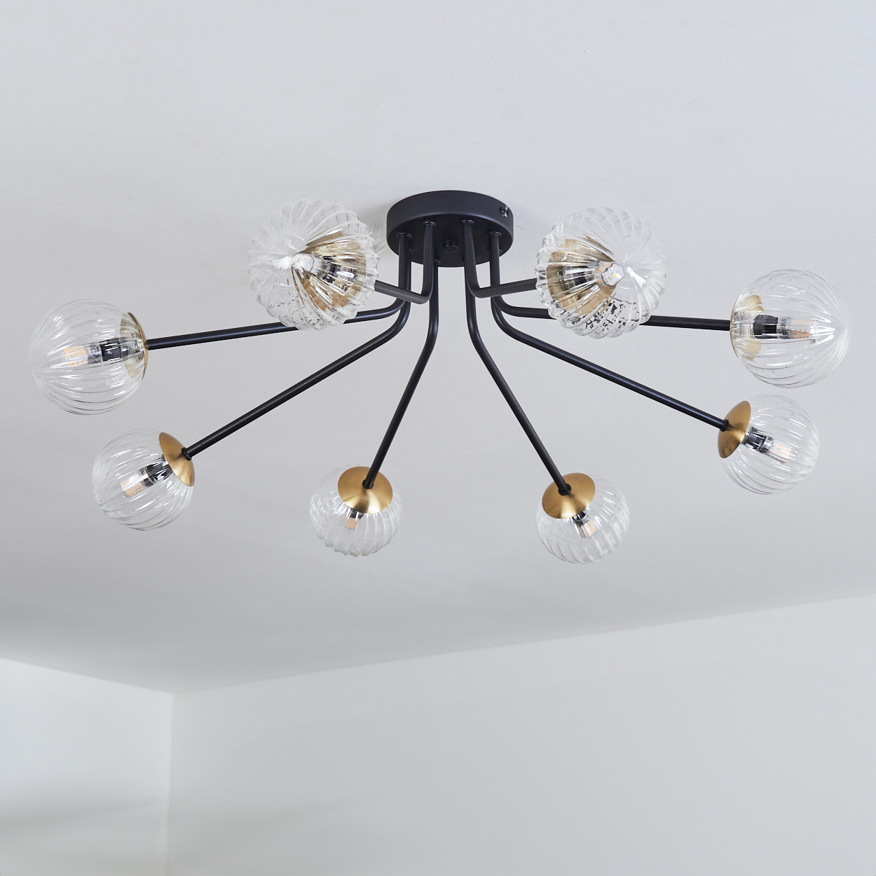 Eine moderne Deckenleuchte mit acht Glaskugeln, schwarzen Armen und goldenen Akzenten, vor einer weißen Decke.