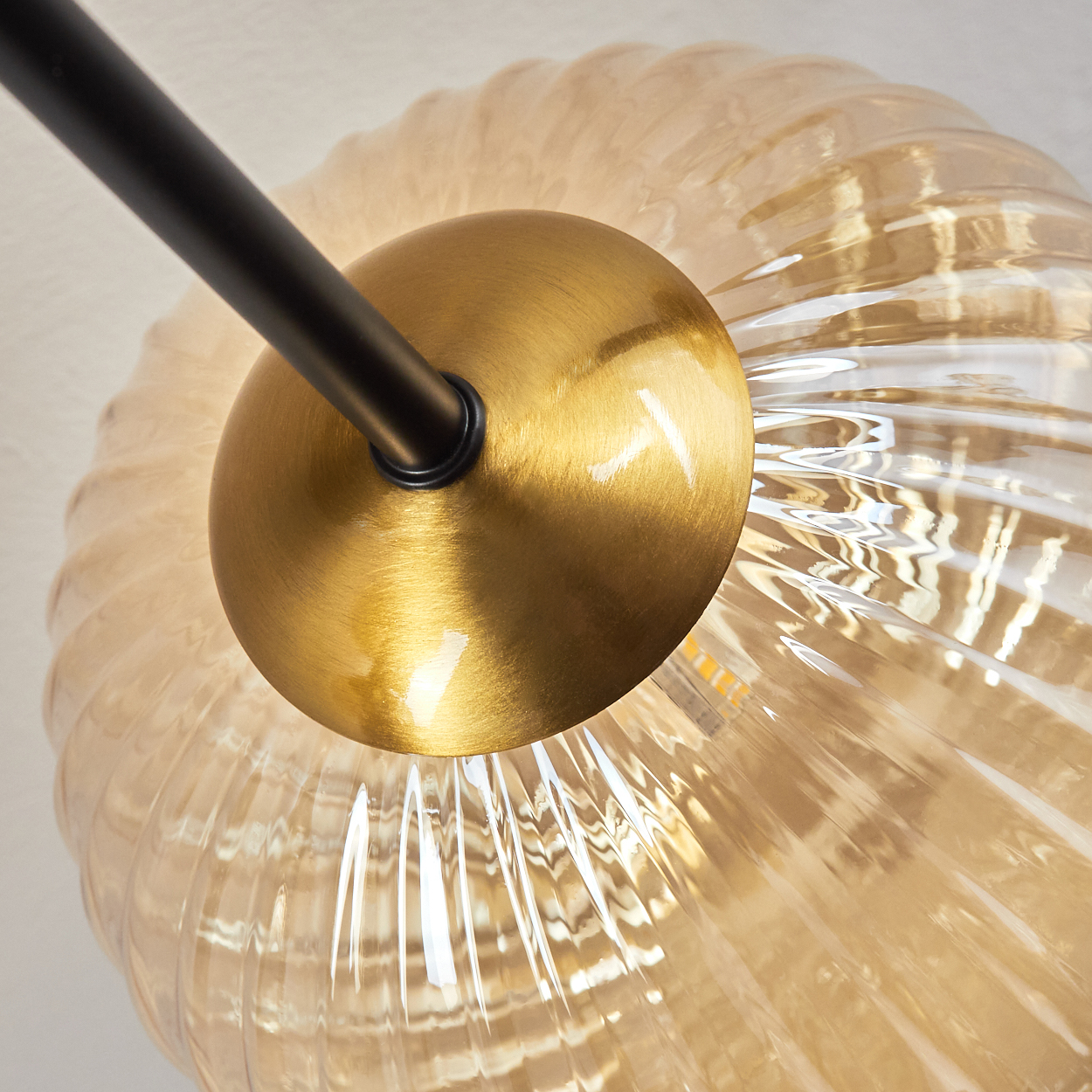 Nahaufnahme einer goldfarbenen Lampenhalterung mit schwarzem Stiel. Die Lampe hat einen gerippten Glasschirm.