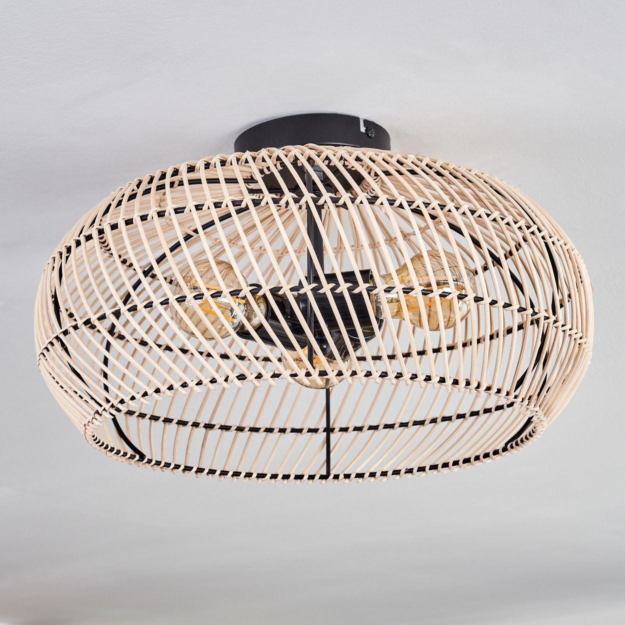Geflochtene Deckenleuchte aus Rattan mit drei Glühbirnen. Das Licht hängt an einer schwarzen Basis an einer weißen Decke.