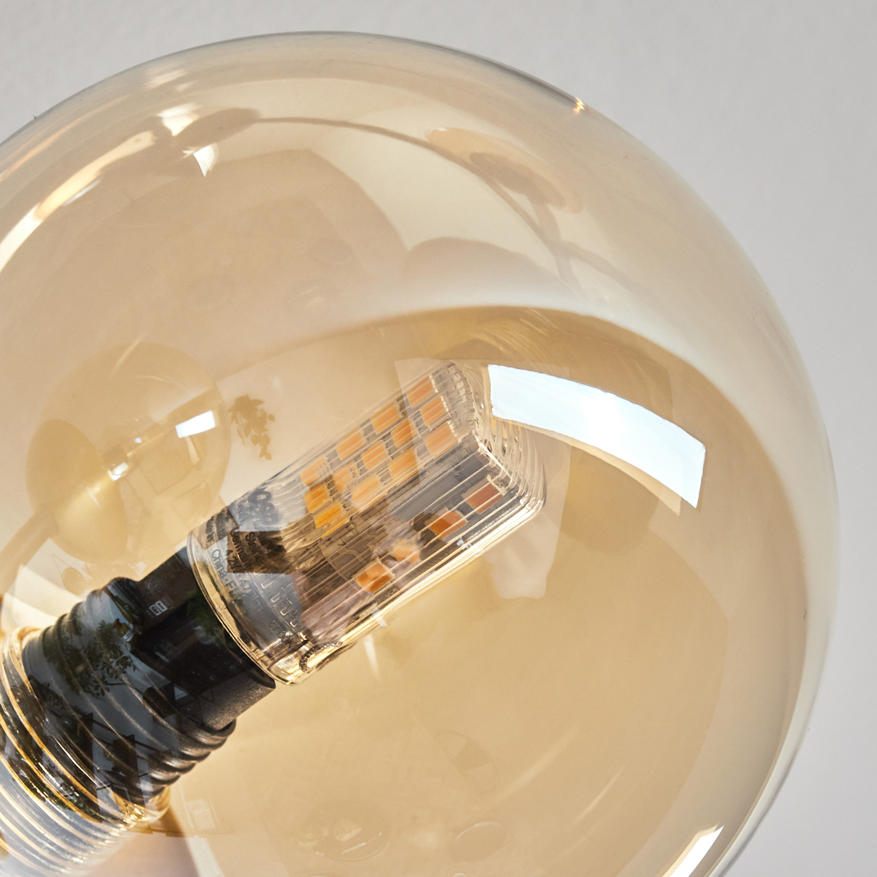 Nahaufnahme einer großen, runden Glühbirne mit klarer Glashülle und einer orangefarbenen LED-Lichtquelle.