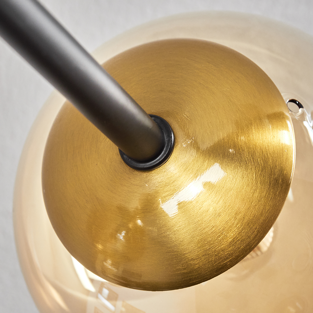 Nahaufnahme einer modernen Lampe. Sie hat einen goldfarbenen Sockel, einen schwarzen Metallarm und eine klare Glaskugel.