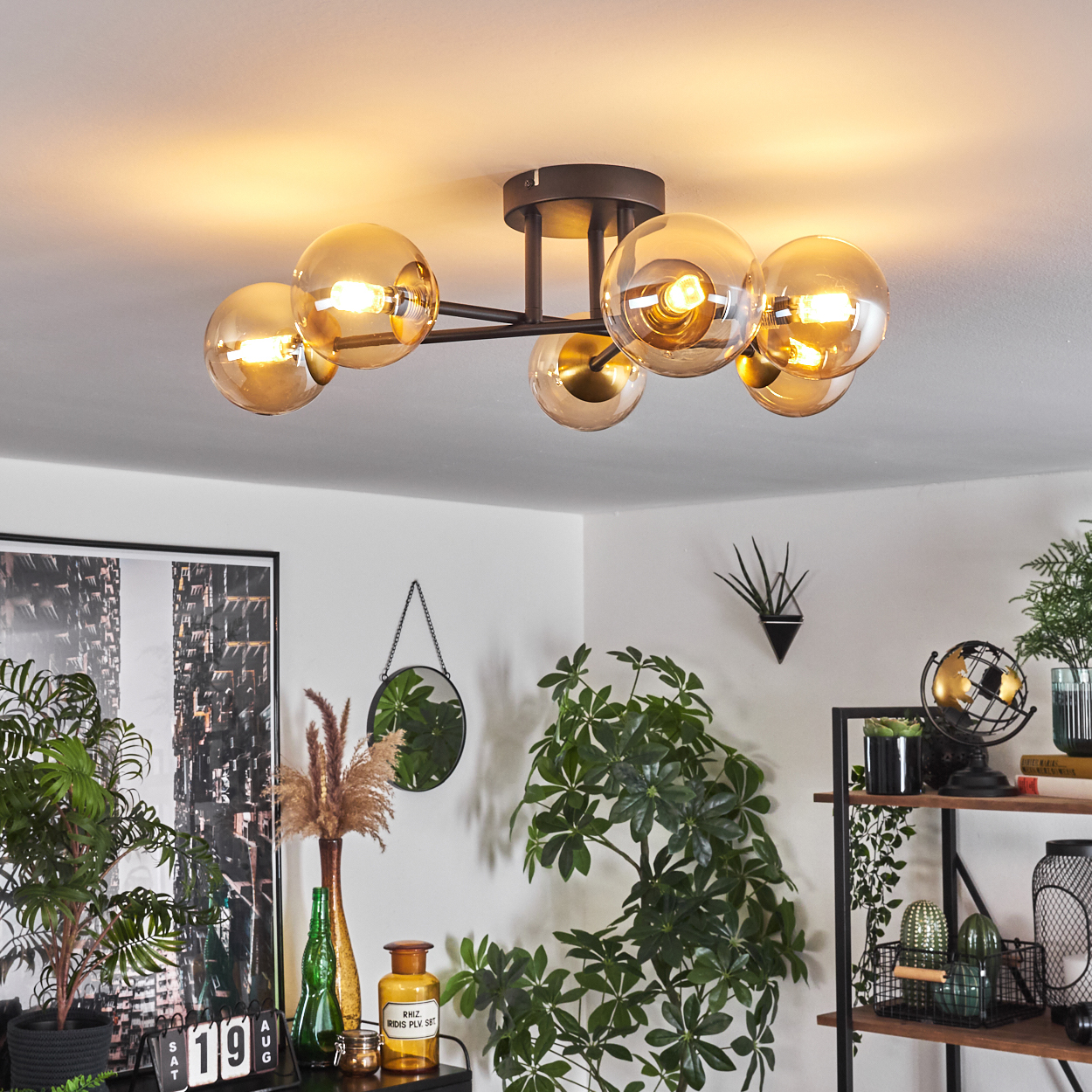 Eine moderne Deckenleuchte mit bernsteinfarbenen Glaskugeln. Pflanzen und Dekoration sind im Raum sichtbar, mit einem Gemälde an der Wand.