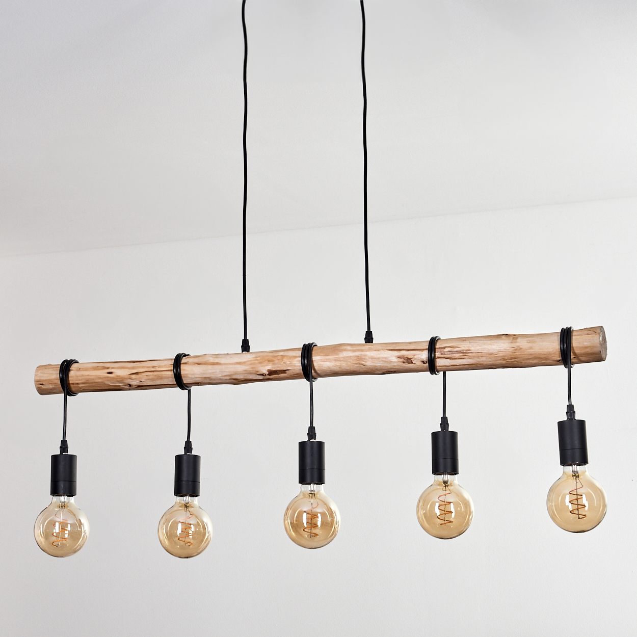 Eine Holzbalken-Kronleuchter mit fünf Edison-Glühbirnen hängt von der Decke. Schwarze Drähte und Halterungen kontrastieren mit dem Holz und der weißen Wand.