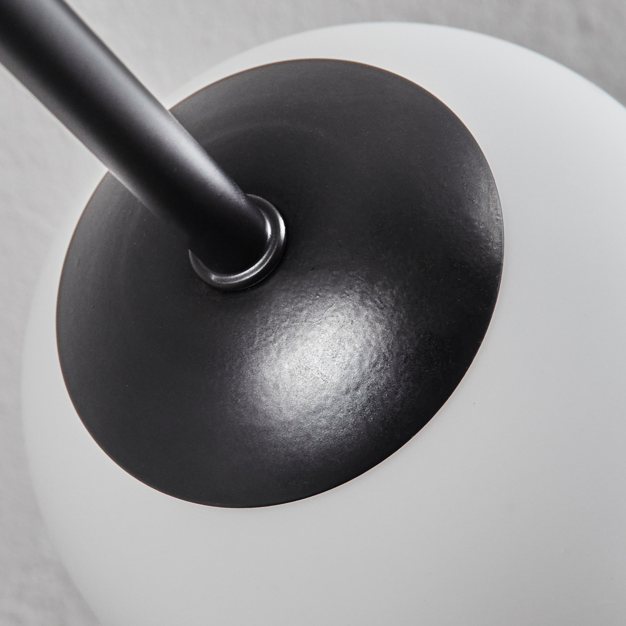 Nahaufnahme einer modernen Lampe. Sie hat einen schwarzen Metallarm und einen kugelförmigen weißen Glasschirm. Die Lampe steht vor hellem Hintergrund.