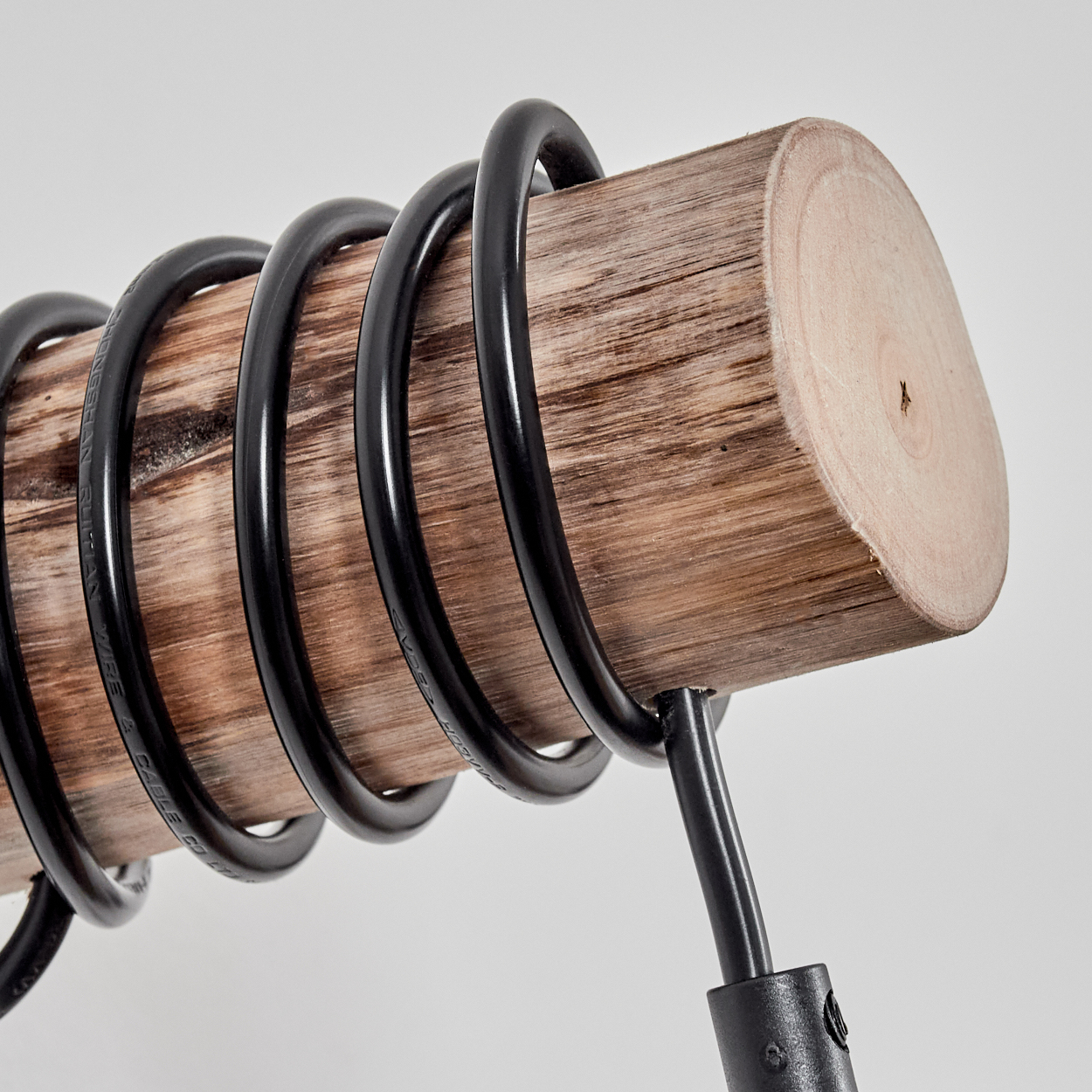 Ein Holzstamm mit schwarzen Metallringen umwickelt. Das Ende des Stammes ist sichtbar und wird von einem schwarzen Metallständer getragen.