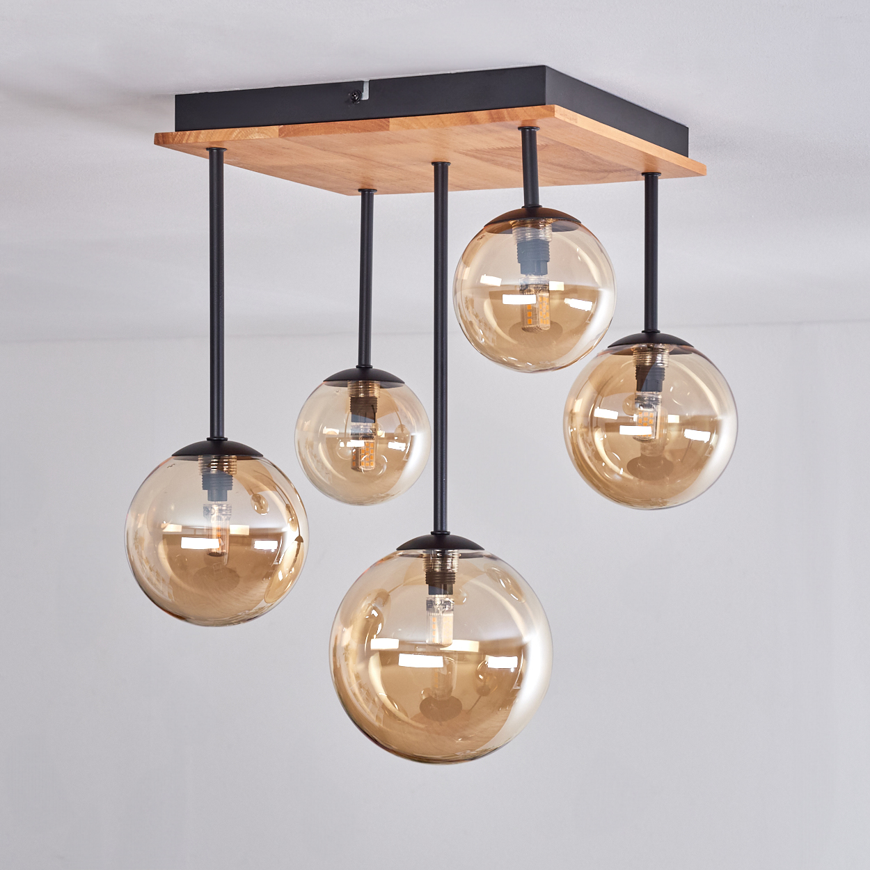 Eine Deckenlampe mit Holz- und schwarzem quadratischem Sockel, mit fünf bernsteinfarbenen Glaskugelschirmen, die an schwarzen Stäben hängen.