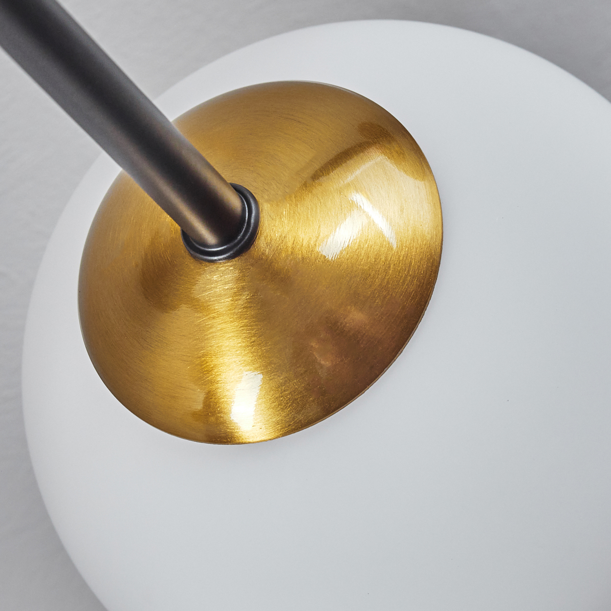 Nahaufnahme einer weißen Kugelleuchte mit goldfarbenem Metallsockel und dunklem Metallstiel auf weißem Hintergrund.