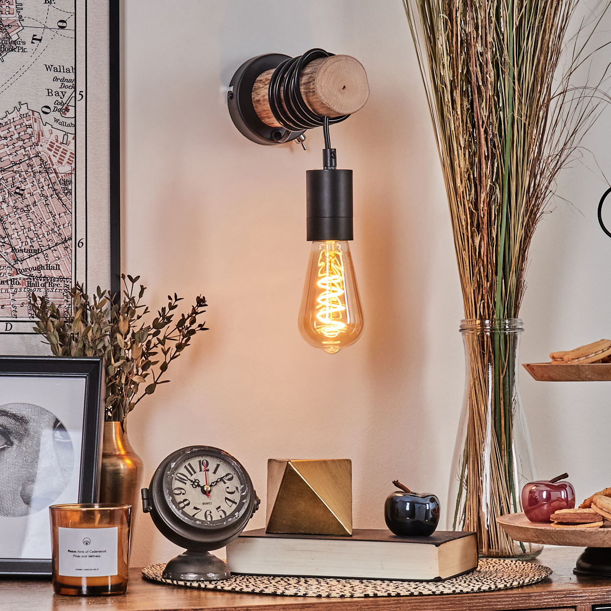 Eine Edison-Glühbirnenlampe ist montiert. Auf einem Tisch befinden sich eine Uhr, Bücher und andere Dekorationen. Im Hintergrund sind eine Karte und getrocknete Pflanzen.