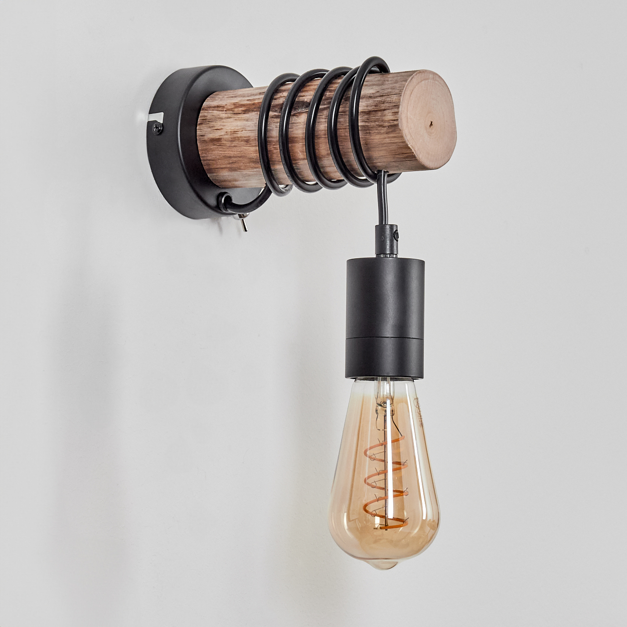 Eine Wandleuchte. Sie hat einen Holzbalken mit Metallspulen, eine schwarze Halterung und eine tropfenförmige Glühbirne.