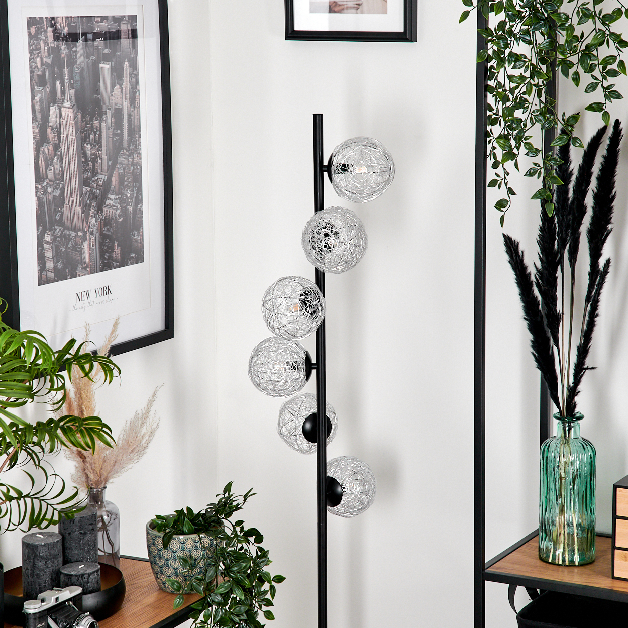 Ein modernes Interieur mit Lampe, Pflanzen und einem gerahmten New York-Bild. Die Lampe hat kugelförmige Drahtschirme.