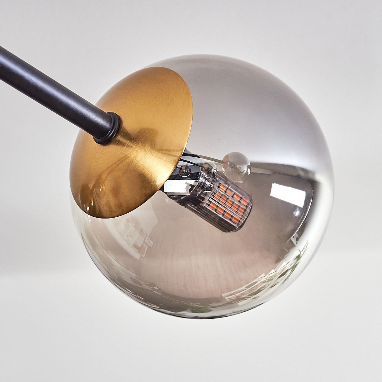 Nahaufnahme einer modernen Lampe. Eine Kugel mit goldenem Akzent und schwarzem Arm. Die Glühbirne hat orangefarbene Lichter. Weißer Hintergrund.