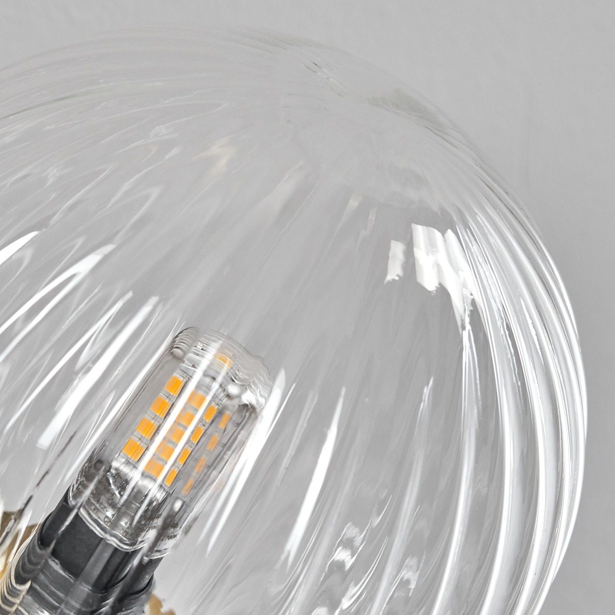 Nahaufnahme einer durchsichtigen, geriffelten Glasbirne. Die Birne hat eine sichtbare LED-Lichtquelle im Inneren, mit grauem Hintergrund.
