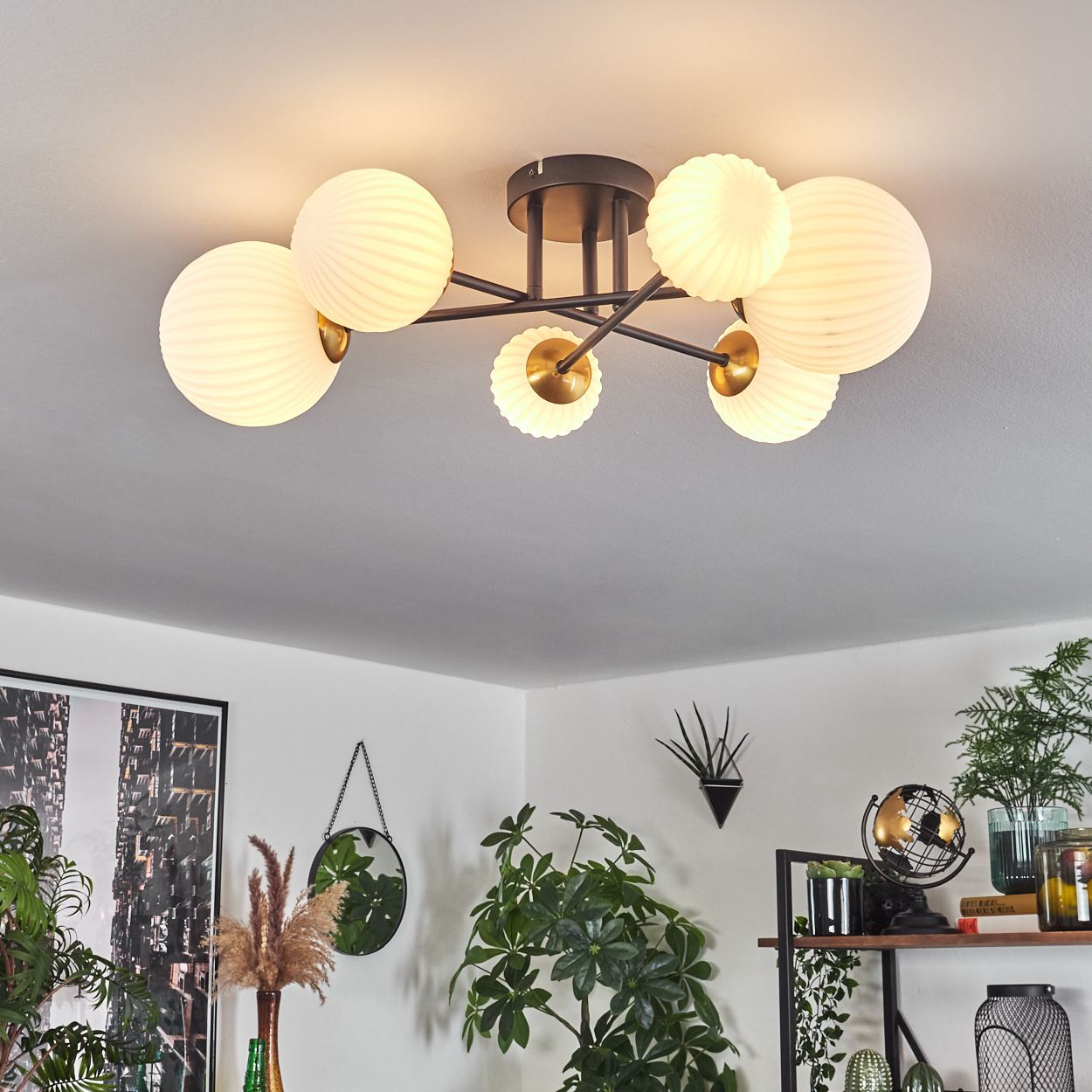 Eine Deckenleuchte mit kugelförmigen Lampen. Der Raum hat Pflanzen, einen Spiegel und ein Regal mit Dekoration.