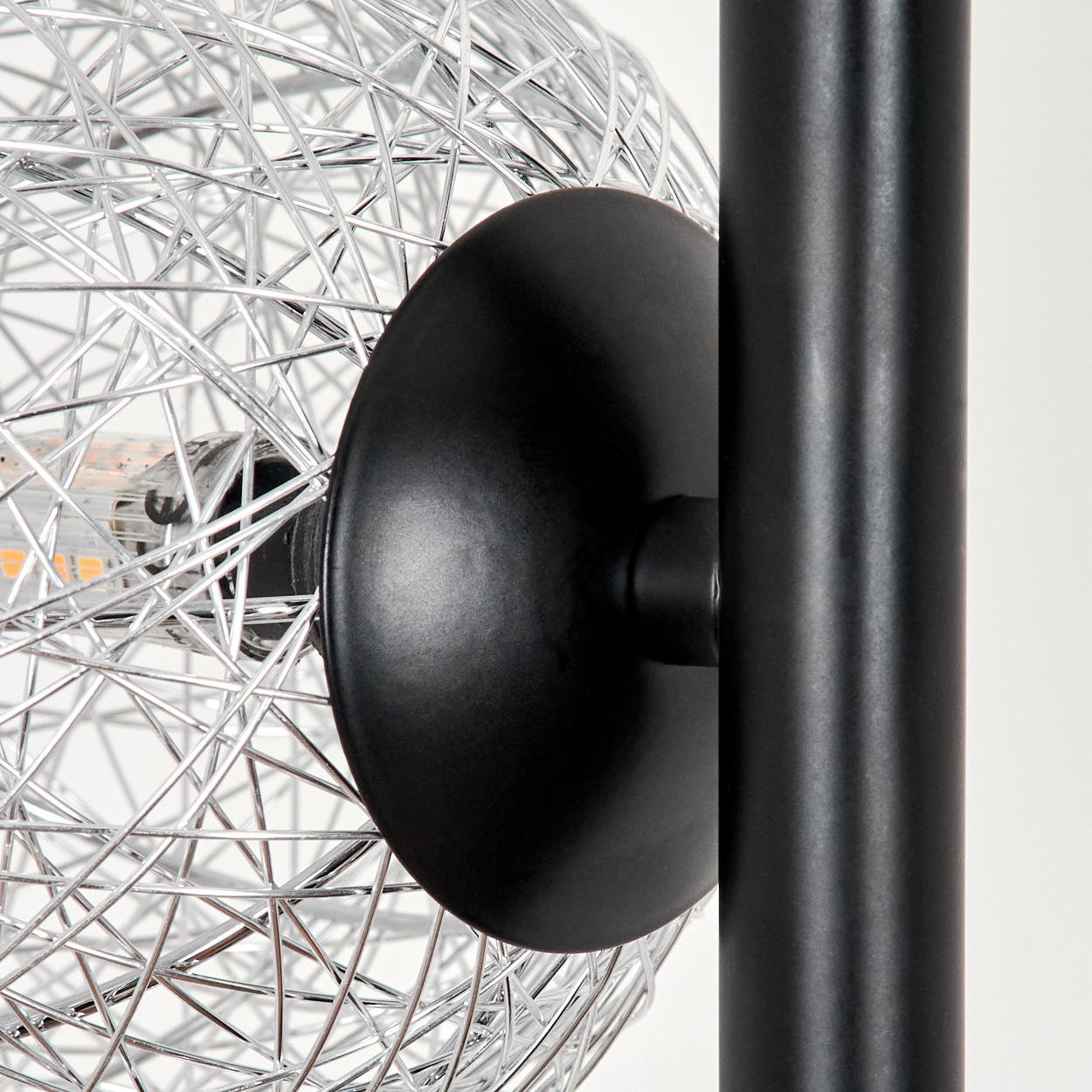 Nahaufnahme einer modernen Lampe. Eine Chromdrahtkugel ist an einer schwarzen Scheibe und einem schwarzen Pfosten befestigt.