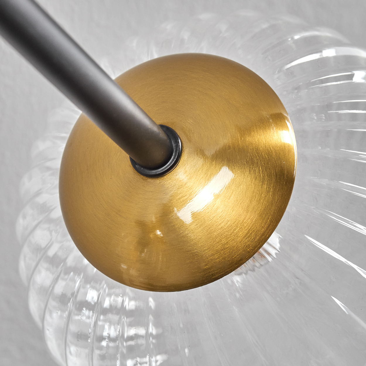 Nahaufnahme einer Leuchte. Eine goldfarbene Scheibe mit einer schwarzen Stange. Klares, geripptes Glas umgibt die Scheibe.