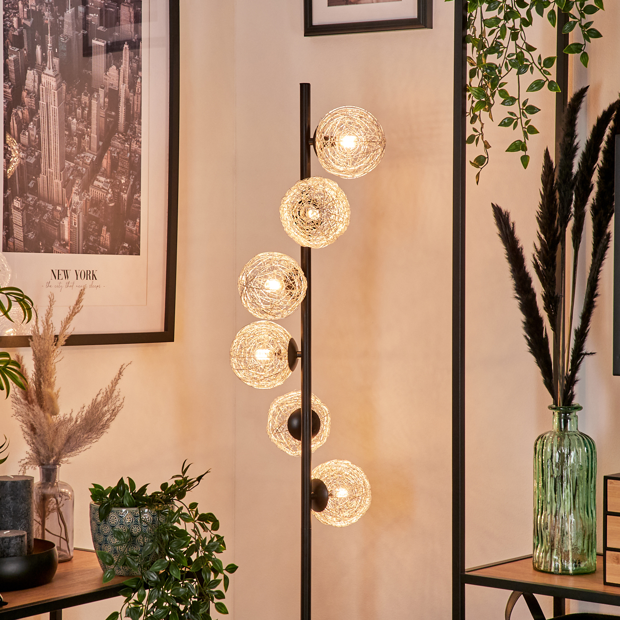 Eine Stehlampe mit sechs kugelförmigen Lichtern. Ein New York-Stadtbild, Pflanzen und Dekorationsartikel sind im Raum.