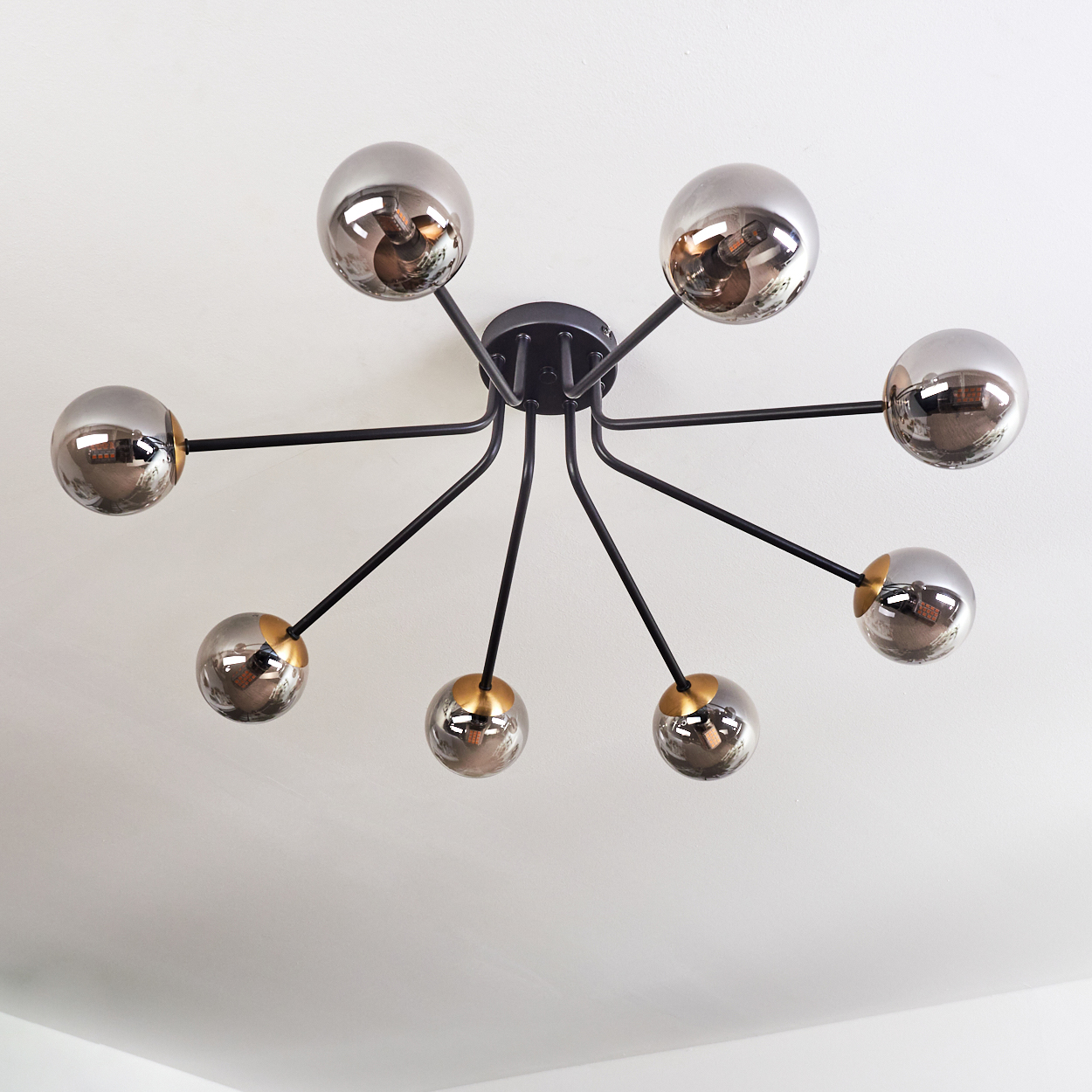 Eine moderne Deckenlampe mit acht kugelförmigen Lichtern. Schwarze Arme erstrecken sich von einem zentralen Sockel mit goldenen Akzenten.