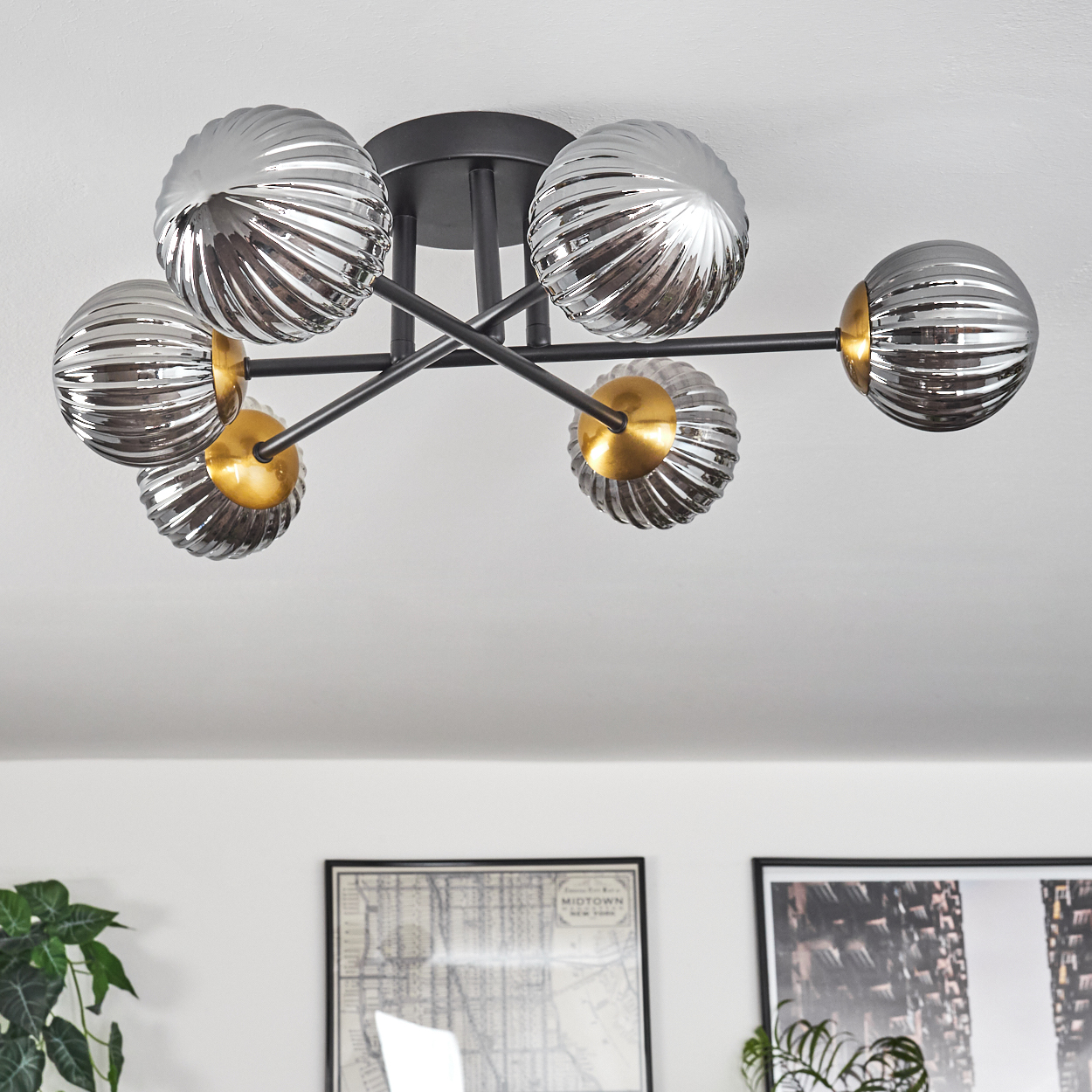 Deckenleuchte mit silbernen Glaskugeln und goldenen Akzenten. Schwarze Metallarme erstrecken sich von einer zentralen Halterung. Zwei gerahmte Bilder unten.