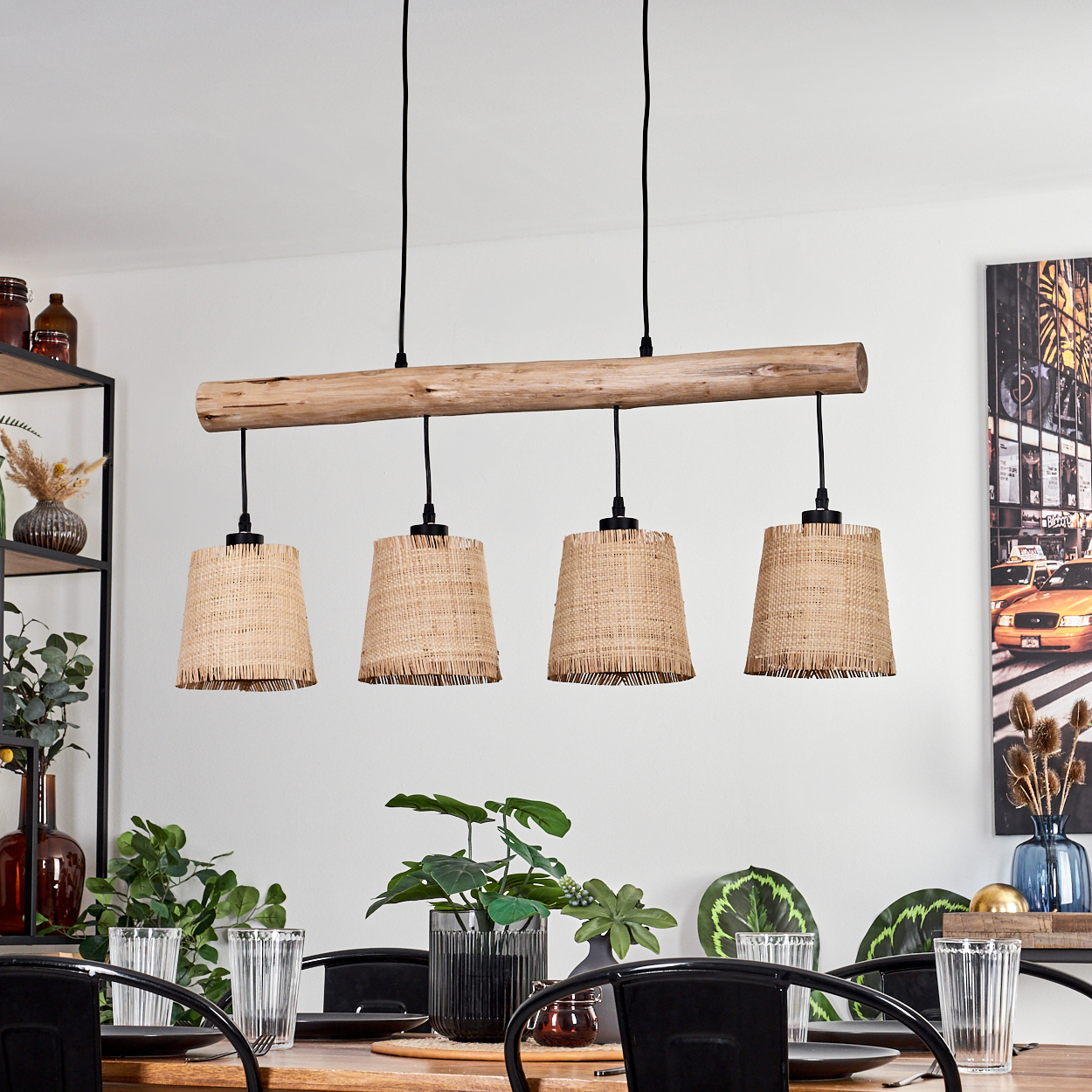 Ein Holzbalken mit vier gewebten Lampen hängt über einem Esstisch. Pflanzen, Gläser und schwarze Stühle vervollständigen die Szene.