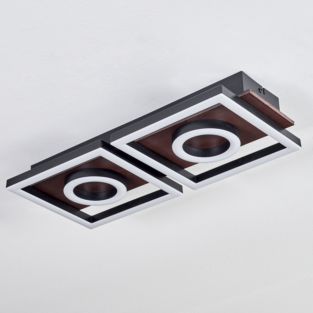 Deckenleuchte mit zwei quadratischen Paneelen, braunem Holz, weißen LED-Umrissen und schwarzen Rahmen, vor weißer Decke.