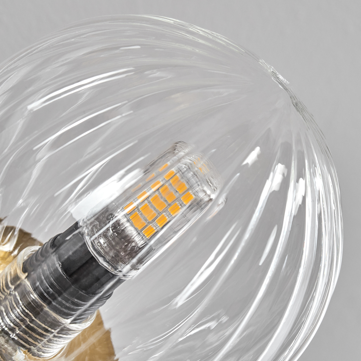 Nahaufnahme einer klaren Glühbirne. Im Inneren befindet sich eine orangefarbene LED-Lampe. Das Glas hat ein Spiralmuster. Grauer Hintergrund.