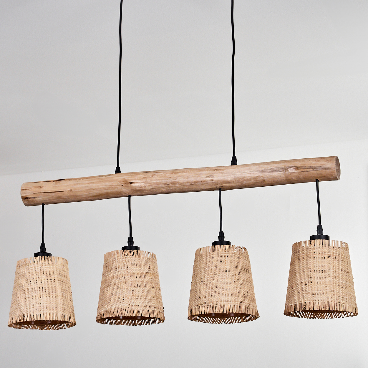 Ein Holzbalken mit vier gewebten Lampen, die darunter hängen. Die Lampenschirme sind konisch, der Hintergrund ist eine weiße Wand.