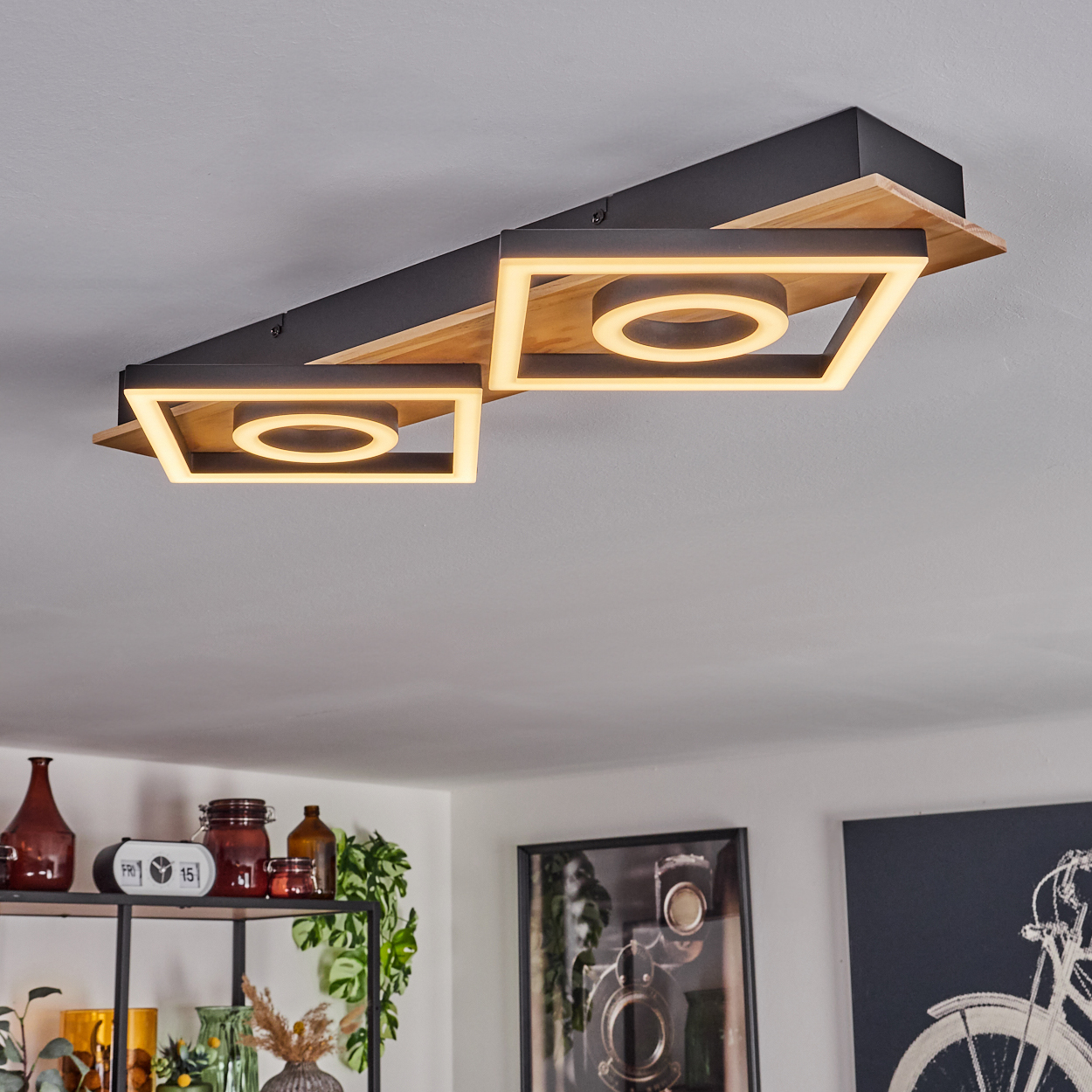 Eine moderne Deckenleuchte mit quadratischen Rahmen und kreisförmigen Lichtern. Der Hintergrund zeigt einen Raum mit Dekor und Kunst.
