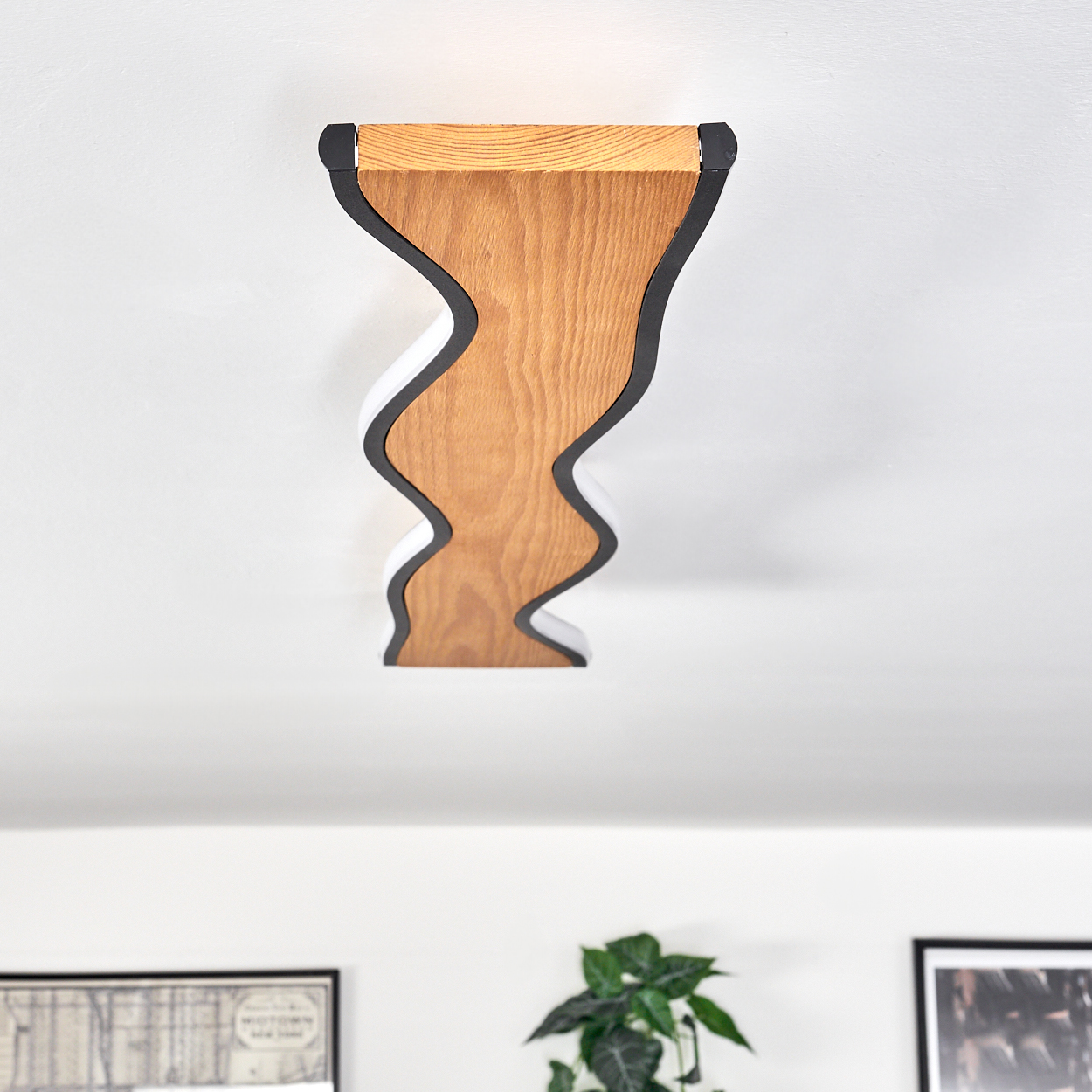 Eine Holzleuchte mit wellenförmigem Design ist an einer weißen Decke befestigt. Schwarze und weiße Akzente umrahmen das Holz.
