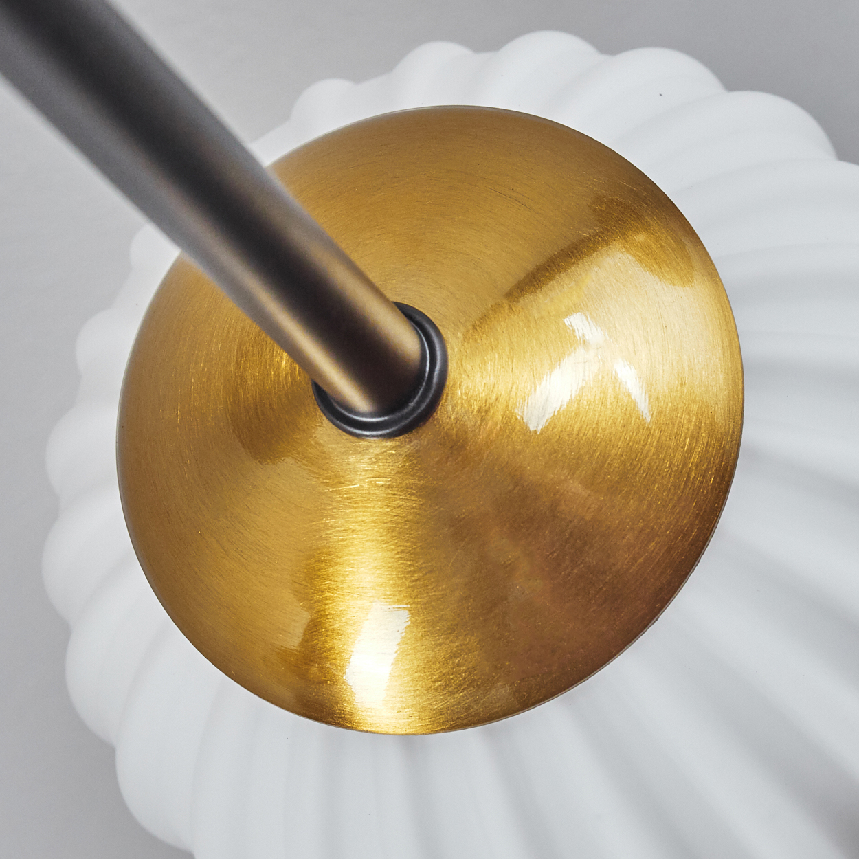 Nahaufnahme einer goldfarbenen Leuchte. Eine dunkle Metallstange ragt aus der Mitte heraus. Die Lampe hat einen weißen, wellenförmigen Sockel.