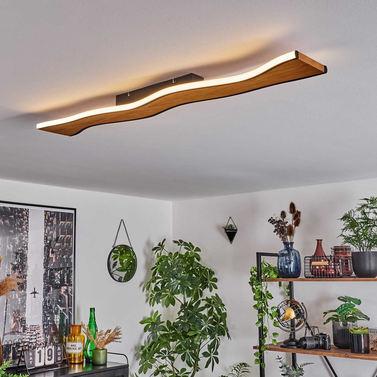 Ein modernes Wohnzimmer mit einer Deckenlampe aus Holz, Pflanzen und Regalen. Ein Spiegel hängt an der Wand, und links ist ein Bild.