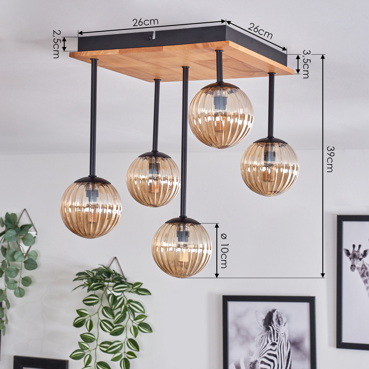 Eine Deckenlampe mit fünf bernsteinfarbenen Glaskugeln hängt an einem Holzsockel. Abmessungen sind enthalten, mit Pflanzen und gerahmter Kunst im Hintergrund.