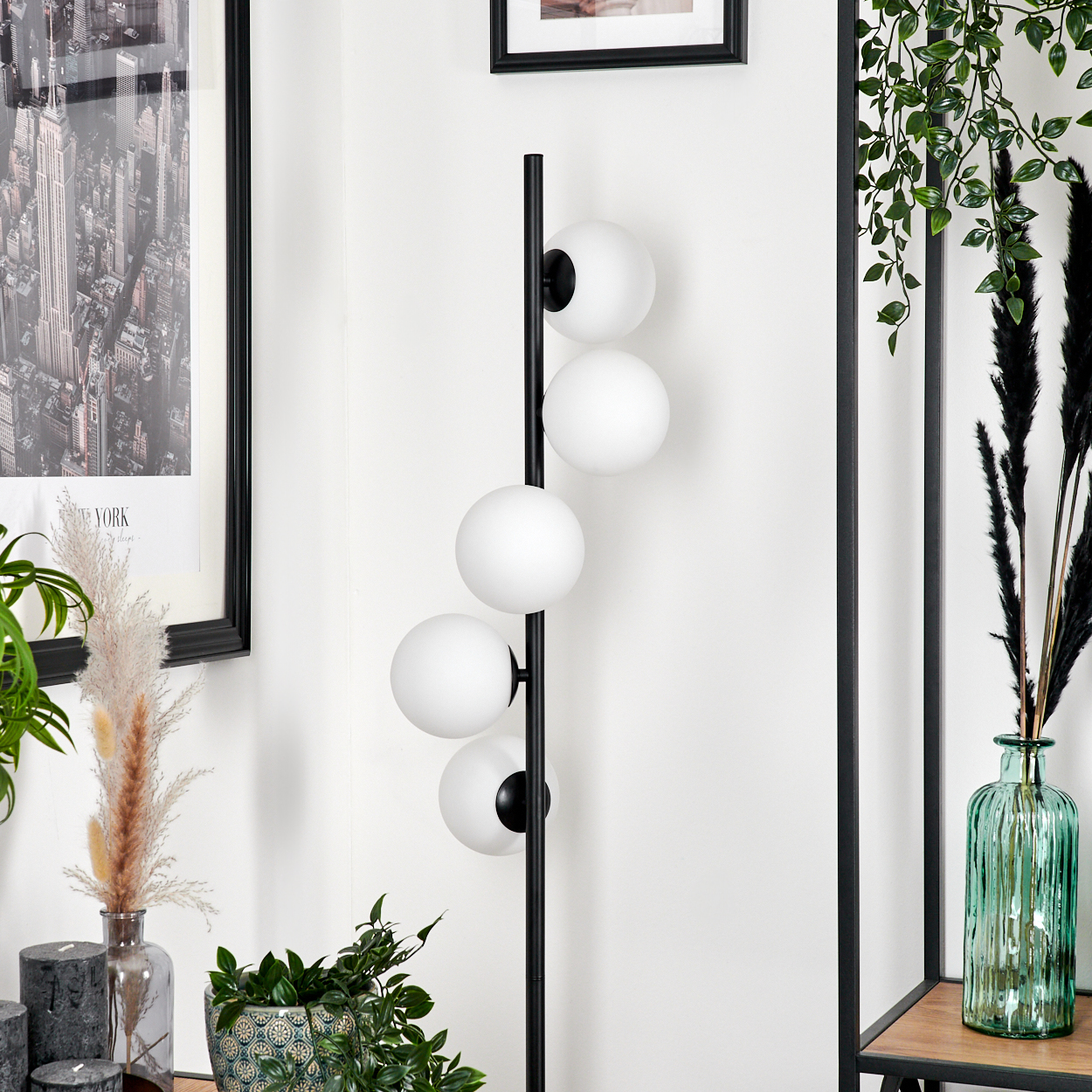 Eine moderne Stehlampe mit vier weißen Kugellampen. Der Hintergrund umfasst gerahmte Kunst, Pflanzen und eine Glasvase.