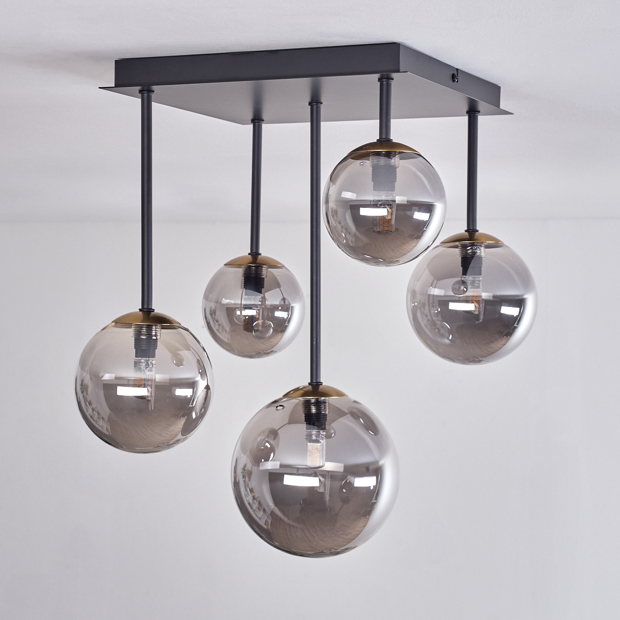 Eine moderne Deckenleuchte mit fünf kugelförmigen, rauchfarbenen Glasschirmen, die von einer schwarzen quadratischen Basis hängen.