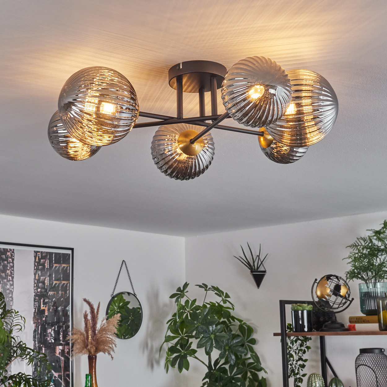 Eine moderne Deckenleuchte mit sechs Glaskugeln, die einen Raum mit Pflanzen und Dekoration beleuchtet. Ein Spiegel und ein Globus sind sichtbar.