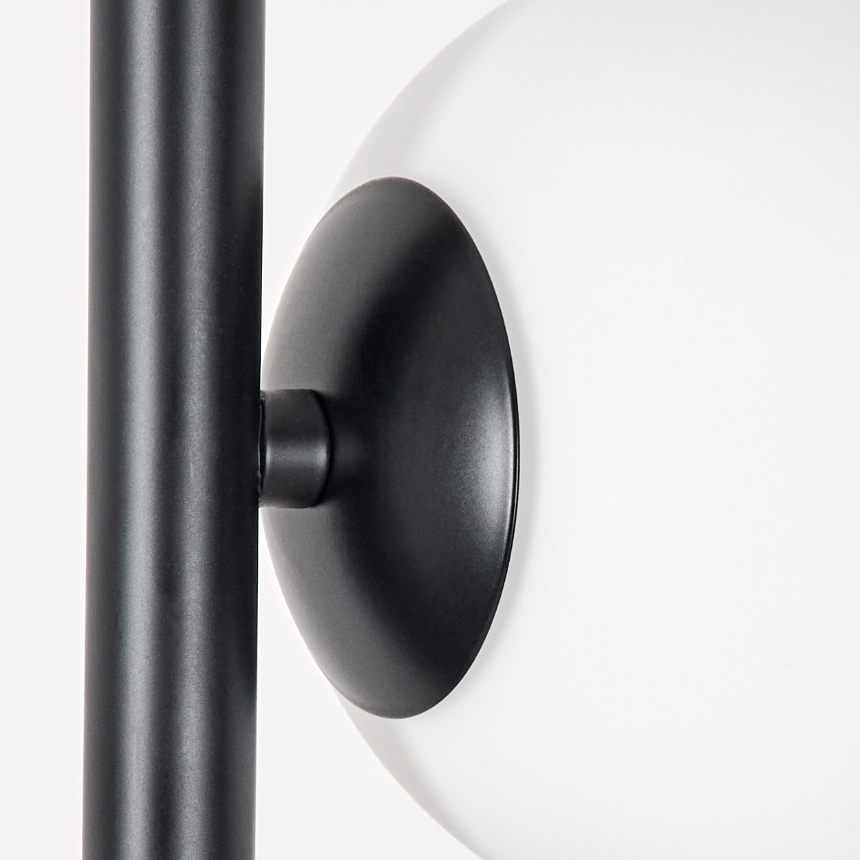 Nahaufnahme einer modernen Lampe. Merkmale: schwarzer Pfosten, schwarze Scheibe und weiße, kugelförmige Leuchte vor weißem Hintergrund.