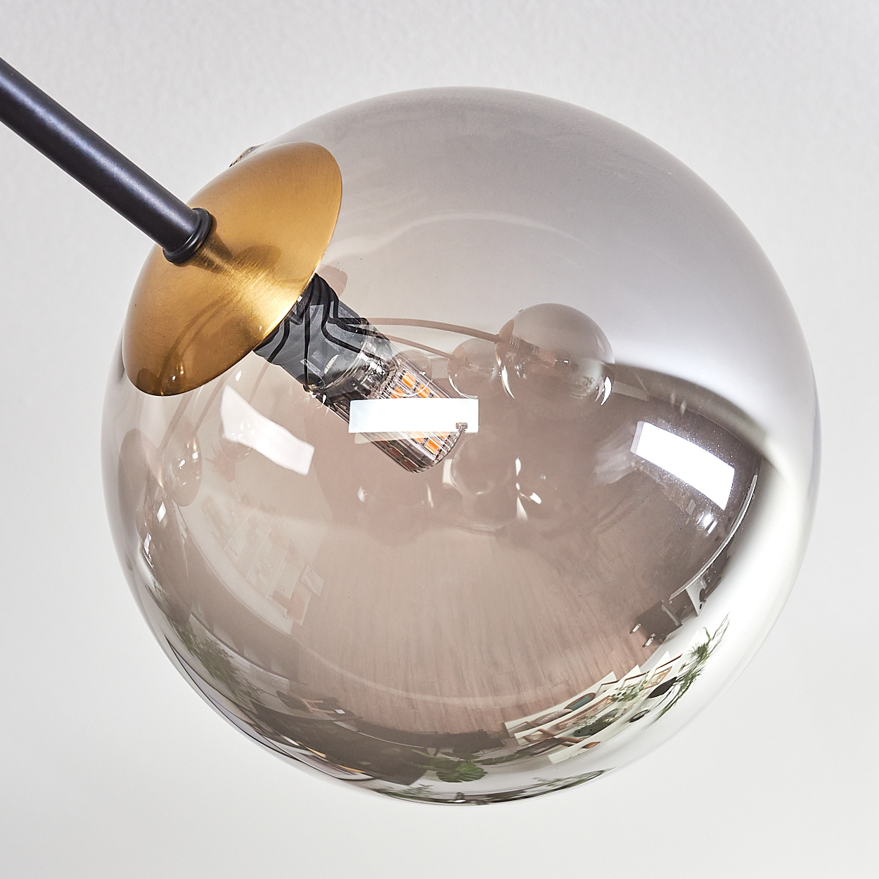 Nahaufnahme einer modernen Lampe mit einer großen, transparenten, grauen Glaskugel. Die Glühbirne ist sichtbar. Der Hintergrund ist weiß.