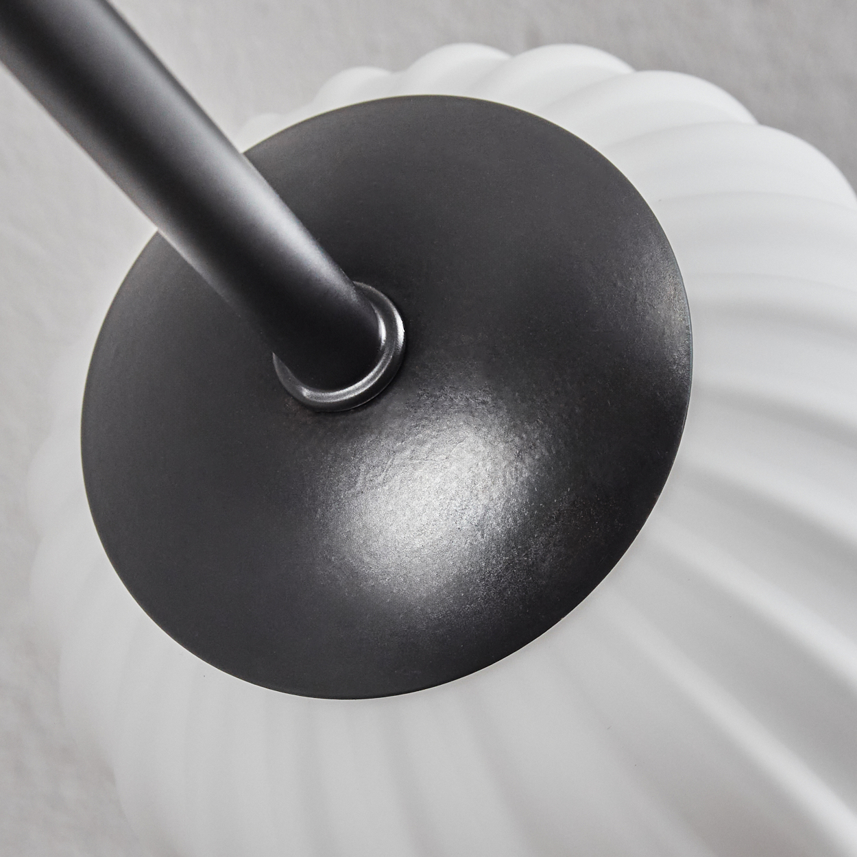 Nahaufnahme einer schwarzen Lampenfassung. Die Lampe hat eine dunkle Metallstange und einen kreisförmigen Sockel. Darunter ist ein weißer, gerippter Glasschirm.